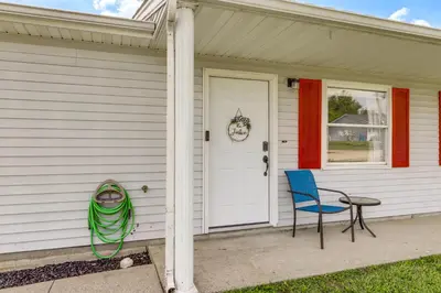 a white house with a table and a blue chair at Quiet Dry Ridge Home with Yard - Near Ark Encounter! in Dry Ridge