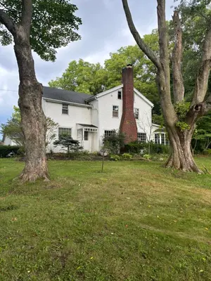 a white house with a brick chimney and trees at Farmhouse Cabin in Ashland