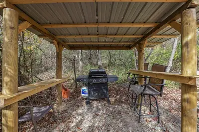 a wooden pergola with a grill in the woods at Cozy Cabin in New Lexington