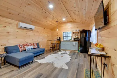 a living room with a blue couch and a kitchen at Stout Cabin with Fire Pit 1 Mi to Ohio River! in Stout
