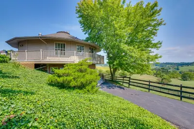 a house on a hill with a fence and a tree at Amish Country Getaway with Pastoral Views! in Millersburg