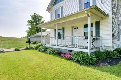 a house with a porch with flowers in the yard at Countryside Home in Wooster with Patio and Fire Pit in Wooster