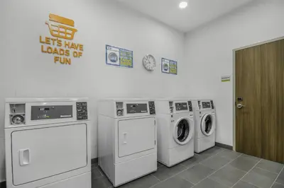 a laundry room with three washing machines and a sign at Home2 Suites By Hilton Cincinnati Midtown Oakley in Cincinnati