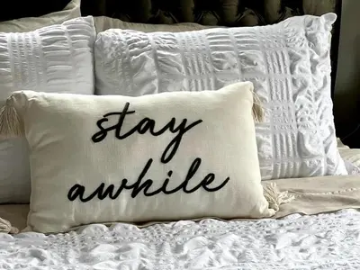 a pillow that says stay awhile on a bed at Home Away From Home - Beautiful Yard in South Euclid