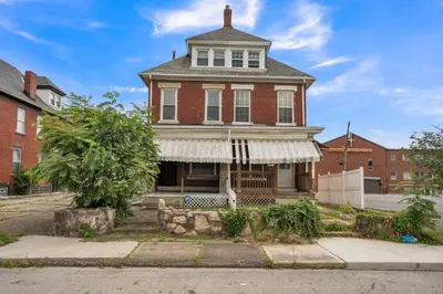 an old red brick house with a white awning at Cozy Renovated 19th Century Home, 5 Min to OSU! in Columbus