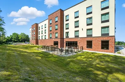 a large brick building with a grass field in front at Cobblestone Hotel & Suites - Bellefontaine in Bellefontaine