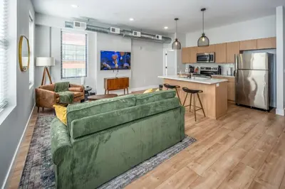 a living room with a green couch and a kitchen at Prime OTR, 1 Block to TQL, Cali King Bed, Sleeps 4ppl, Free Light Rail, Smart TVs in Over-The-Rhine