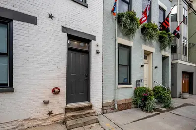 a black door on a white brick building with flags at Prime OTR, 1 Block to TQL, Cali King Bed, Sleeps 4ppl, Free Light Rail, Smart TVs in Over-The-Rhine