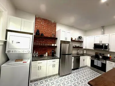 a kitchen with white cabinets and a brick wall at Downtown Adams in Sandusky