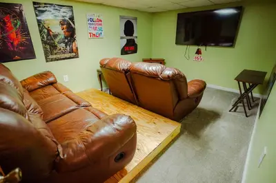 a living room with a brown leather couch and a flat screen tv at Blue Heron Cottage with Game Room, Deck, Hot Tub in Logan