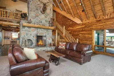 a living room with leather furniture and a stone fireplace at Stunning Cedar Log Home with Panoramic Views - Hot Tub - Game Bar & Theatre Rooms in Coshocton