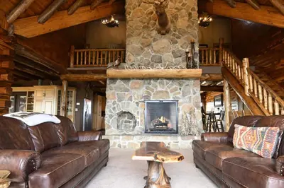 a living room with leather couches and a stone fireplace at Stunning Cedar Log Home with Panoramic Views - Hot Tub - Game Bar & Theatre Rooms in Coshocton