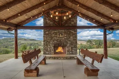 a patio with benches and a stone fireplace at Stunning Cedar Log Home with Panoramic Views - Hot Tub - Game Bar & Theatre Rooms in Coshocton