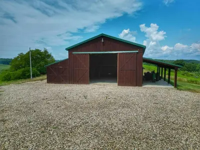a red barn sitting on top of a gravel field at Stunning Cedar Log Home with Panoramic Views - Hot Tub - Game Bar & Theatre Rooms in Coshocton