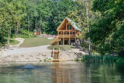 a log cabin on the shore of a lake at Stone Lake Lodge - Lakeside Cabin - Stocked Pond in Coshocton