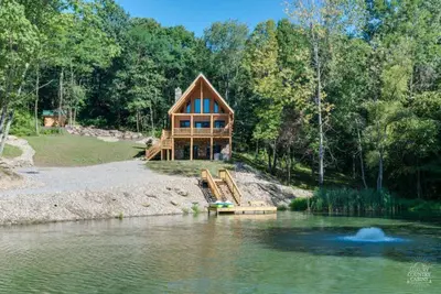 a house on the shore of a lake at Stone Lake Lodge - Lakeside Cabin - Stocked Pond in Coshocton