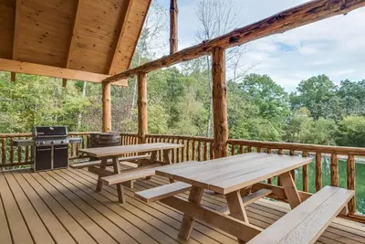 a wooden deck with picnic tables and a grill at Stone Lake Lodge - Lakeside Cabin - Stocked Pond in Coshocton
