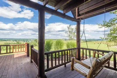 a porch swing with a view of a field at Coschocton Hills - 2 Luxury Log Cabins - Lake in Coshocton
