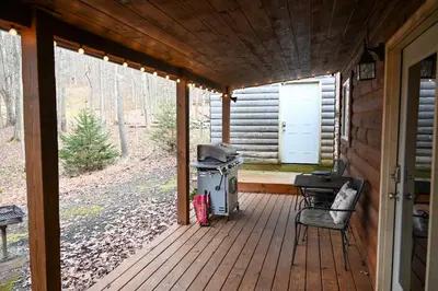 a porch of a cabin with a grill and a chair at A Beary Cozy Cabin in Hocking Hills in Laurelville