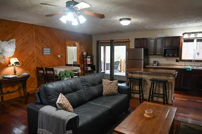 a living room with a black leather couch and a kitchen at A Beary Cozy Cabin in Hocking Hills in Laurelville