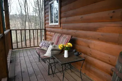 a porch with a bench and a table with flowers at A Beary Cozy Cabin in Hocking Hills in Laurelville