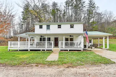 a white house with a porch and an american flag at On 220 Acres! Hot Tub Haven in West Liberty in West Liberty
