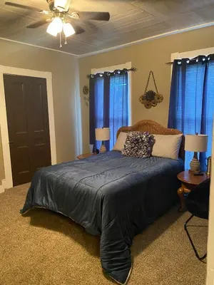 a bedroom with a bed with blue curtains and a ceiling fan at Charming Wheeling Island Home in Wheeling