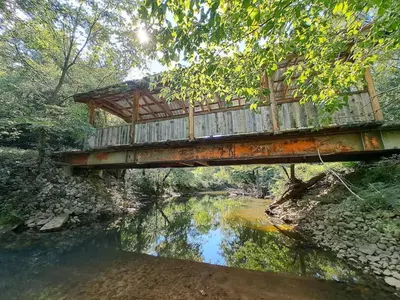 a bridge over a river with a reflection in the water at Covered Bridge Hideaway, swimming hole hot tub in Stanton