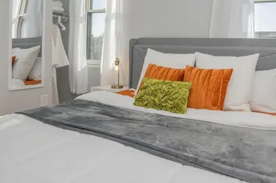 a white bed with orange and green pillows on it at Sleep like a King - OTR- Free Light Rail ! in Cincinnati