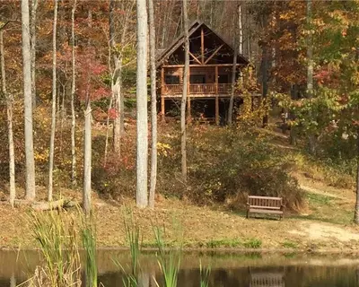 a wooden cabin in the woods with a bench next to a lake at The Secluded Woodbury Cabin, Pond and 42 acres in Warsaw