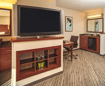 a hotel room with a large television and a desk at Hyatt Place Cincinnati Blue Ash in Blue Ash