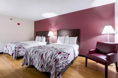 a hotel room with two beds and a chair at Red Roof Inn Carrollton in Carrollton
