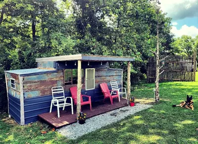 a cabin with chairs and a porch with a dog at Cozy Tiny House on Working Farm, for Fun Glamping Trips in Kentucky in Owenton