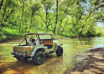 a green jeep driving through a river at Cozy Tiny House on Working Farm, for Fun Glamping Trips in Kentucky in Owenton