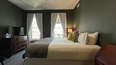 a bedroom with a bed and a tv and two windows at Stone Gables Inn in Cleveland
