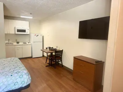 a small room with a bed and a table and a refrigerator at Siegel Select Cincinnati Sharonville in Cincinnati