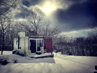 a snow covered cabin with two chairs and a table in the snow at Rustic Container Accommodation for Glamping in Kentucky in Owenton