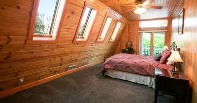a bedroom with wooden walls and a bed in a room with windows at Romantic Forest Cabin with Amazing Private Deck and Spa in Ohio in Sugarcreek