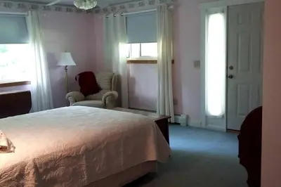 a bedroom with a bed and a chair and windows at Romantic Room Rental on a Lovely Farm near Hillsboro, Ohio