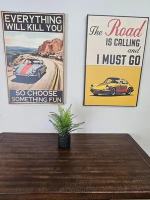 two posters on a wall with a table and a plant at Vroooom . . . . the ROAD is calling. . . . in Trenton