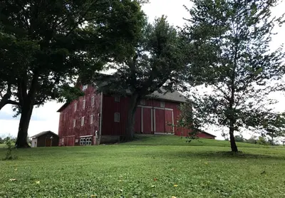 a red barn in a field with two trees at Stunning Rustic Converted Barn Country Getaway near Wabash, Indiana in Wabash