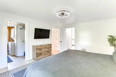 a white bedroom with a large bed and a flat screen tv at 3 Mi to Downtown Youngstown Apt with Deck! in Youngstown