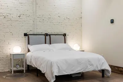 a bedroom with a bed with white sheets and two lamps at Modern Loft-Style Retreat Near Blenko Glass in Milton, WV in Hurricane