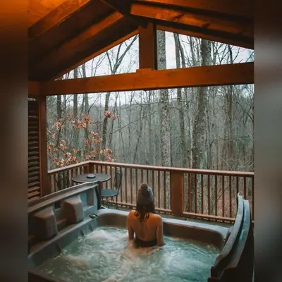 a woman sitting in a hot tub on a porch at A-Frame #02 - by The Chalets in Logan