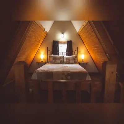 a small attic bedroom with a bed with two lamps at A-Frame #11 - by The Chalets in Logan