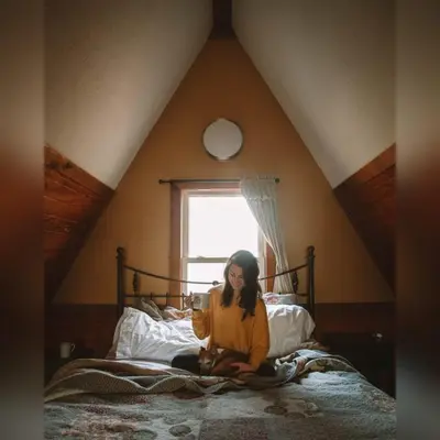 a woman sitting on a bed in a attic at A-Frame #16 - by The Chalets in Logan
