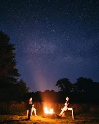 a group of three people sitting around a fire at night at Pine Cone - by The Chalets in Logan