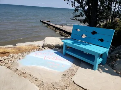 a blue bench sitting on a rock next to the water at Rustic Lakeside Vacation Rental with Beach Access in Vermilion, Ohio in Vermilion