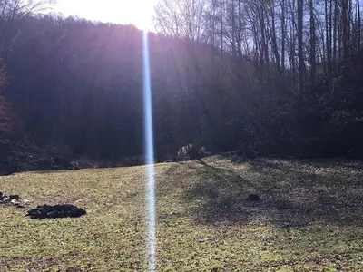 a field with the sun shining through the trees at Stunning Getaway Cabin with Expansive Decks near Huntington, West Virginia in Genoa