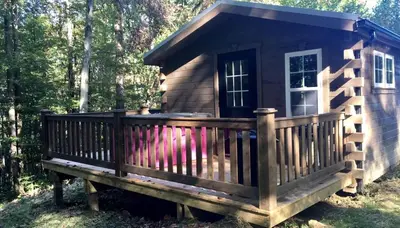 a small cabin with a large deck in the woods at Romantic Log Cabin Accommodation with Private Jacuzzi near Huntington, West Virginia in Genoa